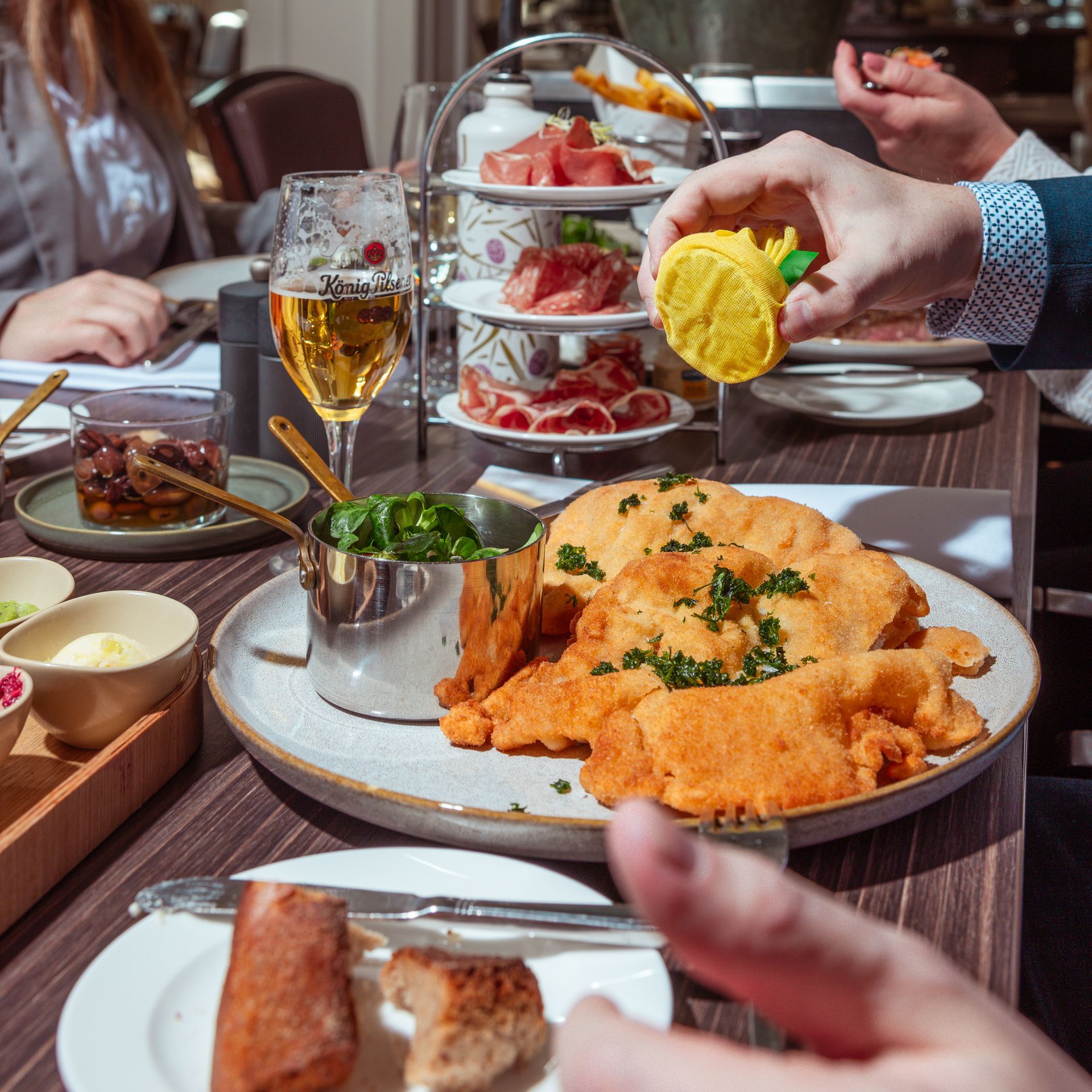 Zwei Personen in Bademänteln liegen Kopf an Kopf auf einem Bett und halten mit den Füßen Champagnergläser.