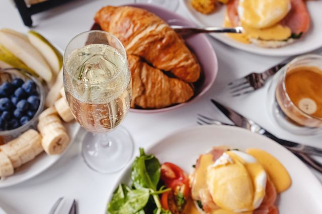 Ein reichhaltiges Frühstücksbuffet mit Croissants, Eggs Benedict, Obst, Kaffee und einem Glas Sekt.