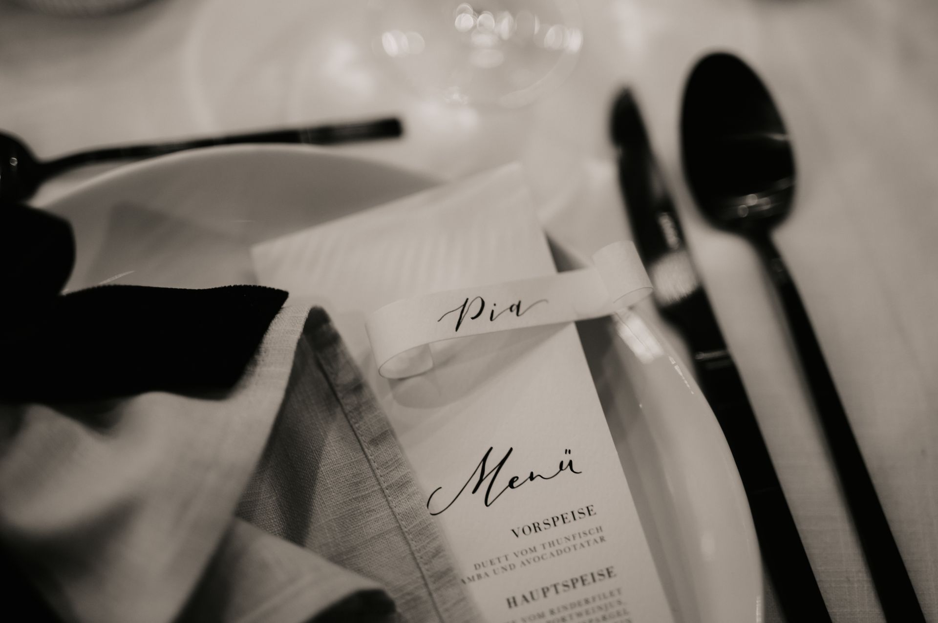 Gedeckter Platz mit Menükarte, Namensschild, schwarzem Besteck und gefalteter Serviette.