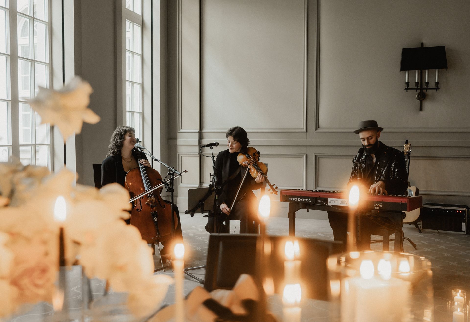 A string trio is playing indoors: cello, violin, and keyboard. Soft lighting, candles.