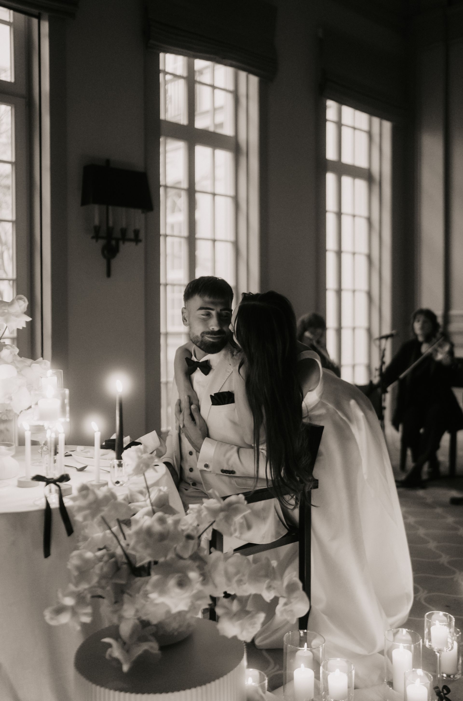 Braut küsst Bräutigam in der Nähe eines mit Kerzen geschmückten Kuchentisches. Im Hintergrund spielt Musik.