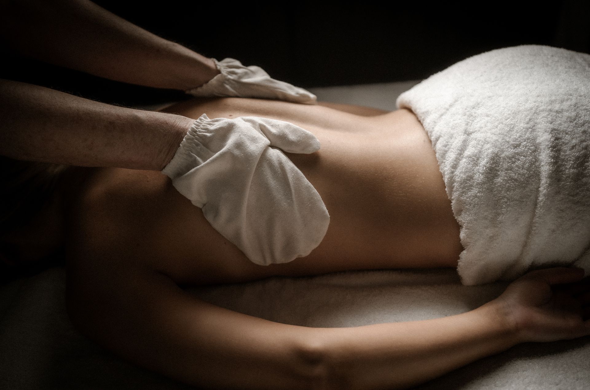 Hände in weißen Handschuhen massieren den Rücken einer Person auf einer Spa-Liege mit einem weißen Handtuch.