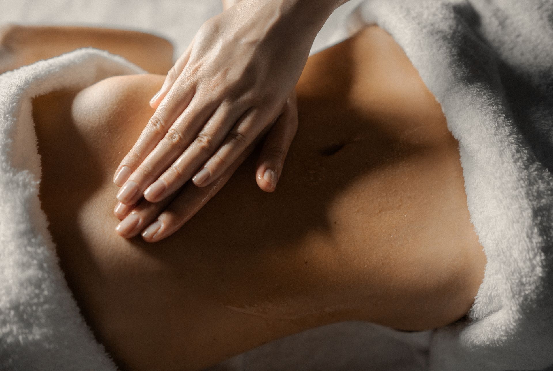 Eine Hand massiert den in ein weißes Handtuch gewickelten Bauch einer Person.