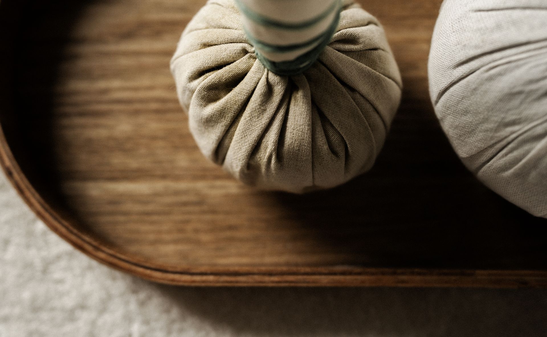 Zwei Kräutermassagekugeln auf einem Holztablett.