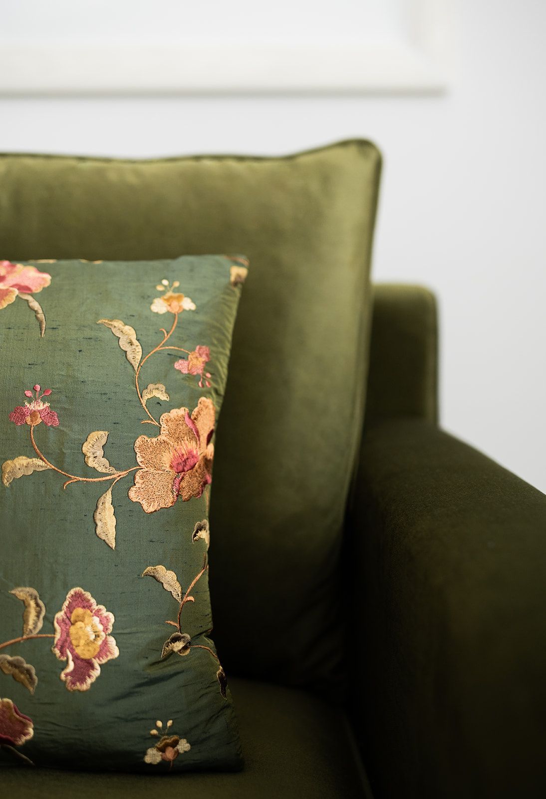 An olive-green sofa with decorative pillows featuring a floral pattern.