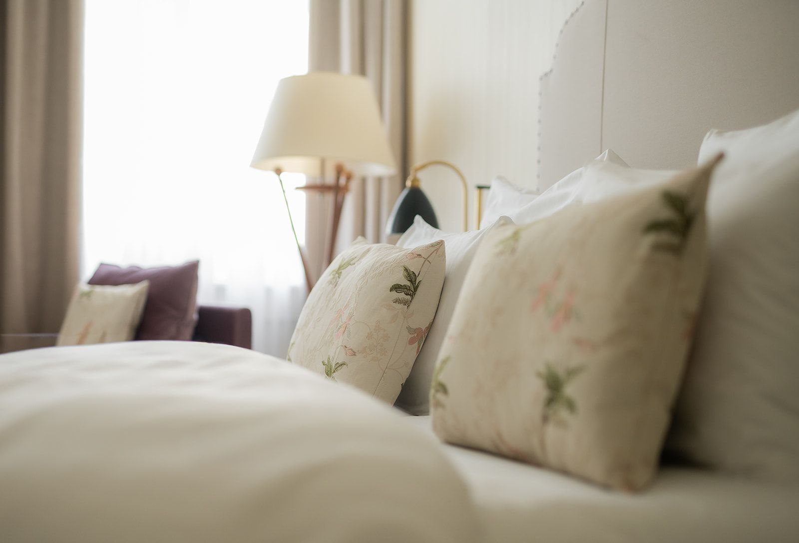 Bett mit geblümten Kissen und einer Lampe in einem hellen Schlafzimmer.