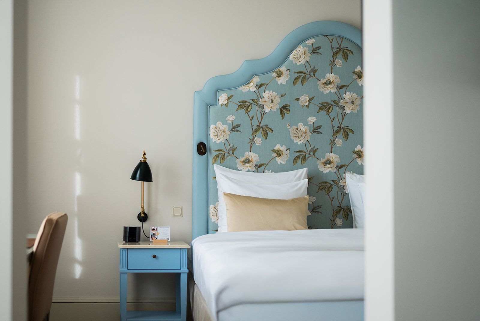 Hotelfassade mit roten Sonnenschirmen, die die Außensitzplätze beschatten. Cremefarbenes Gebäude mit vielen Fenstern und Blumenschmuck.