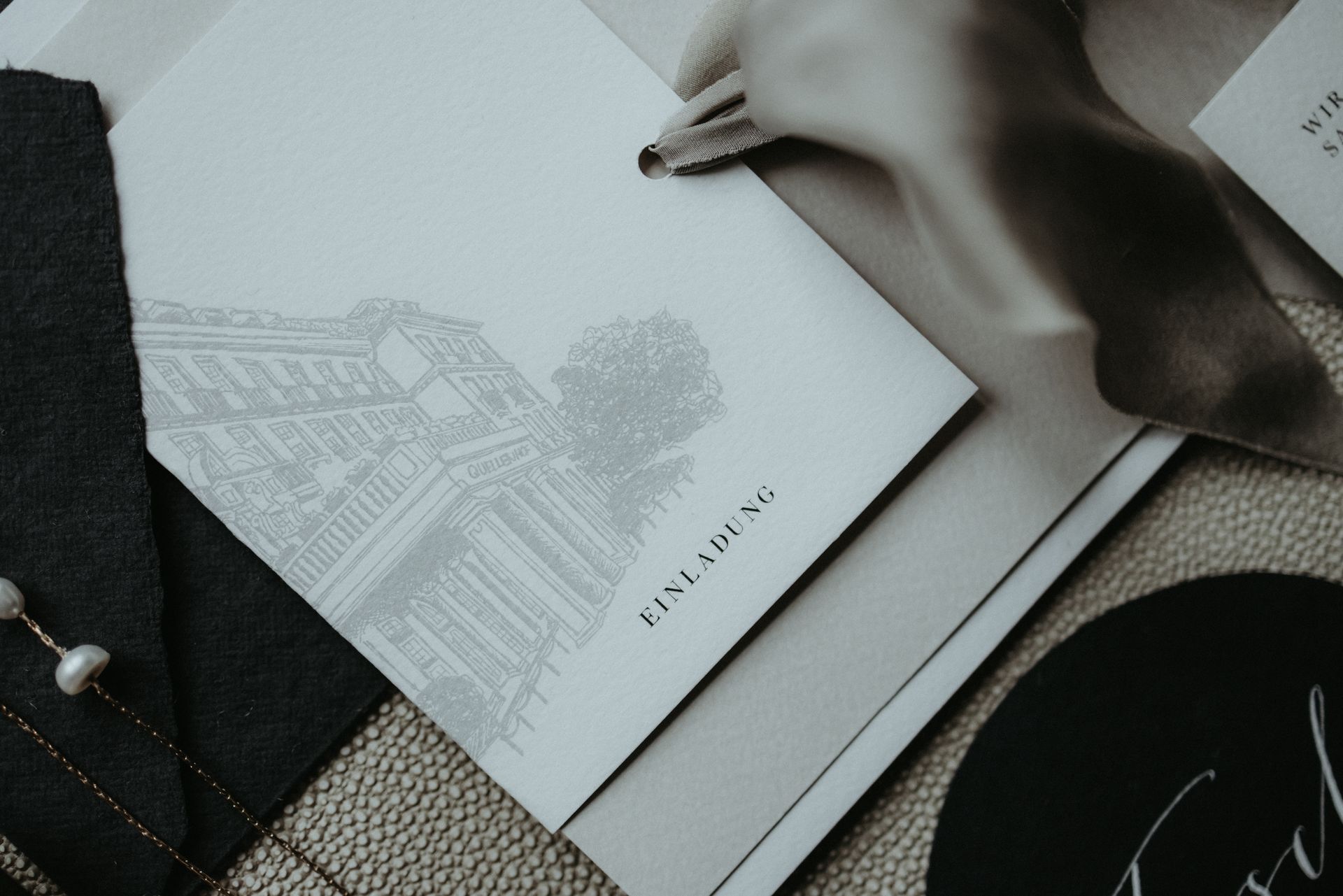 Arrangement aus Schreibwaren mit einer skizzierten Gebäudezeichnung, einem Band und einer Karte. Monochrom.