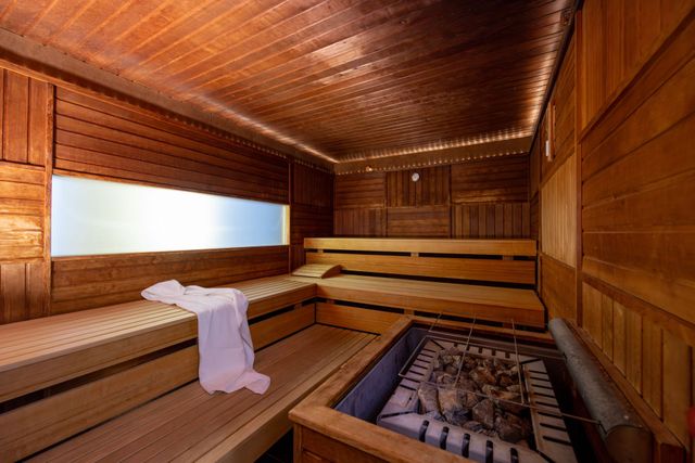 Eine Holzsauna mit gestuften Bänken, einem über einen Sitz drapierten weißen Handtuch und einem mit Steinen gefüllten Ofen.