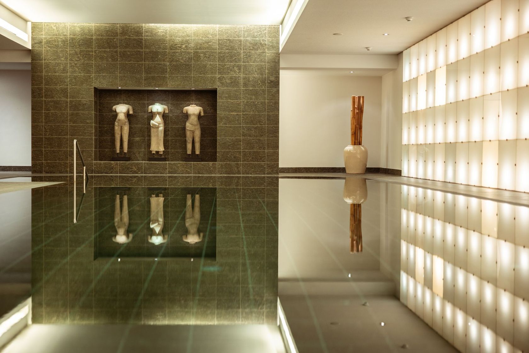 Ein Hallenbad mit Skulpturen, beleuchteten Wandpaneelen und einem vertikalen Holzkunstwerk in einem modernen Ambiente.