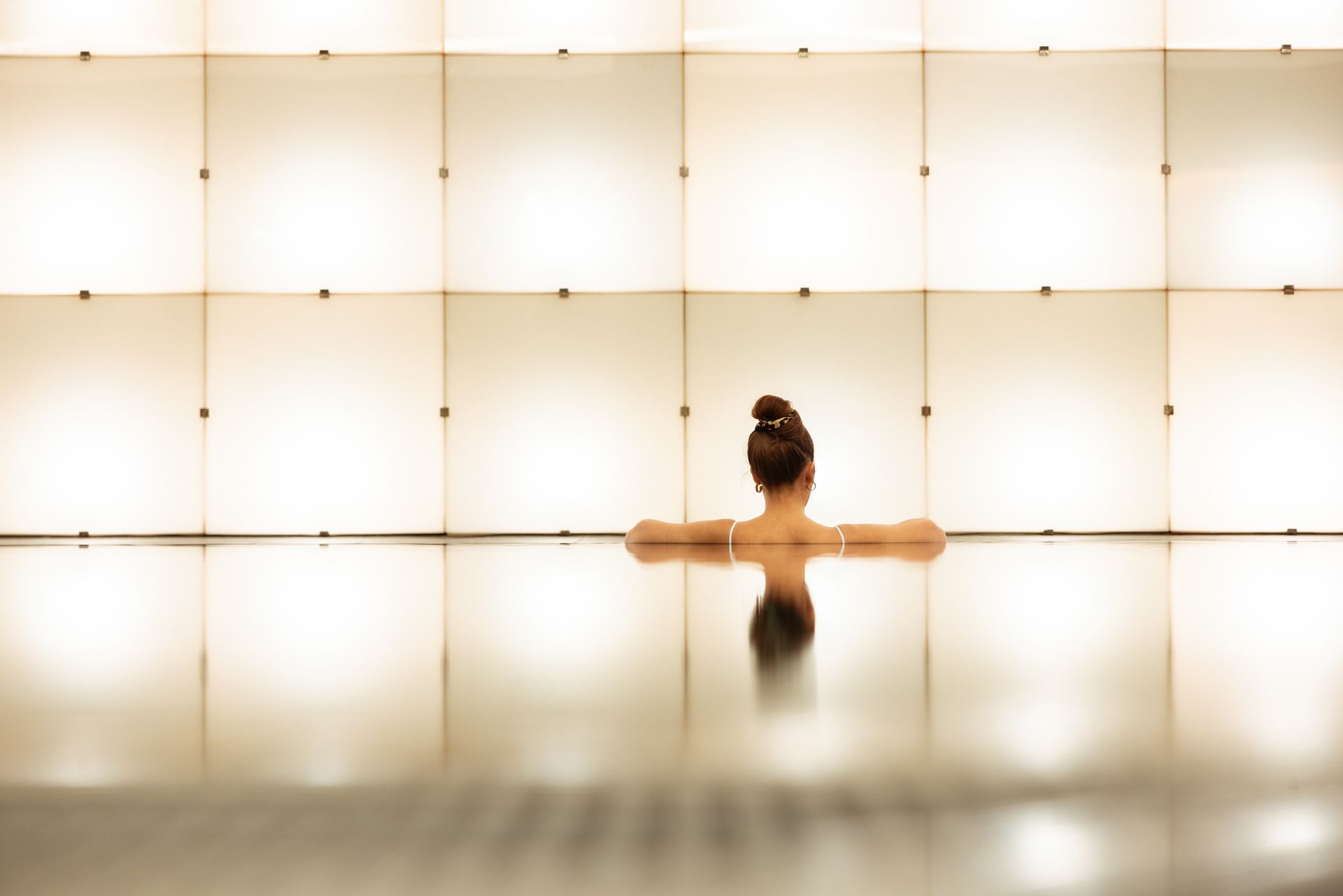 Eine Person ruht in einem ruhigen Innen-Pool vor dem Hintergrund beleuchteter, quadratischer Wandpaneele.