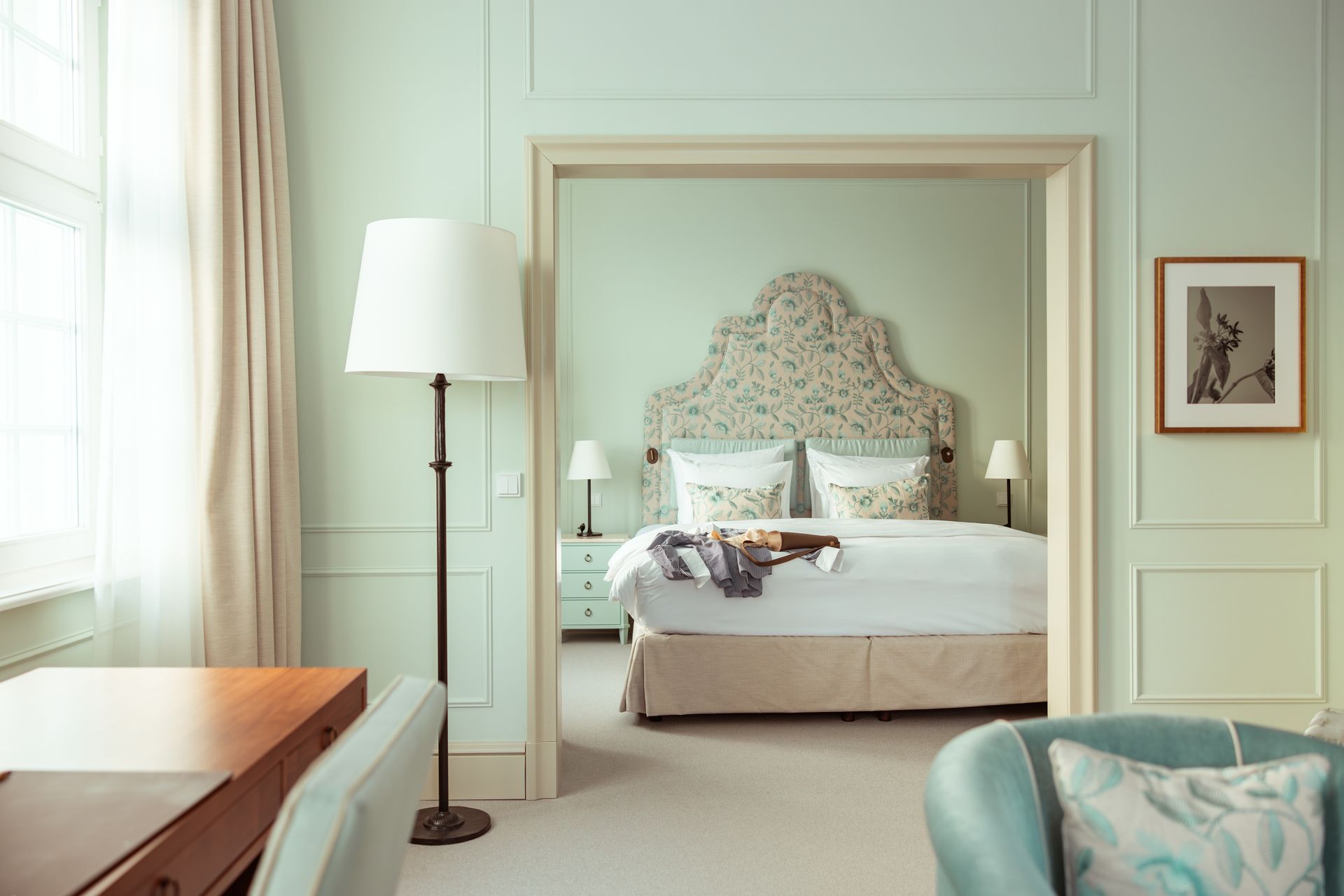 A bedroom interior featuring light green walls, a bed with a floral headboard, and a floor lamp.
