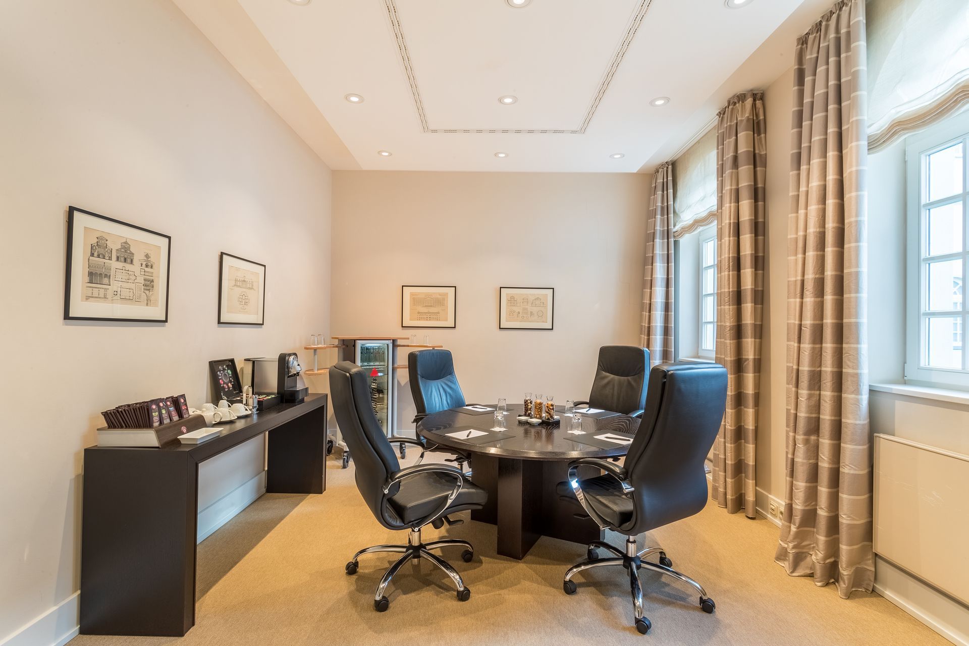 Konferenzraum mit rundem Tisch, schwarzen Ledersesseln und seitlicher Konsole mit Getränken und Snacks.