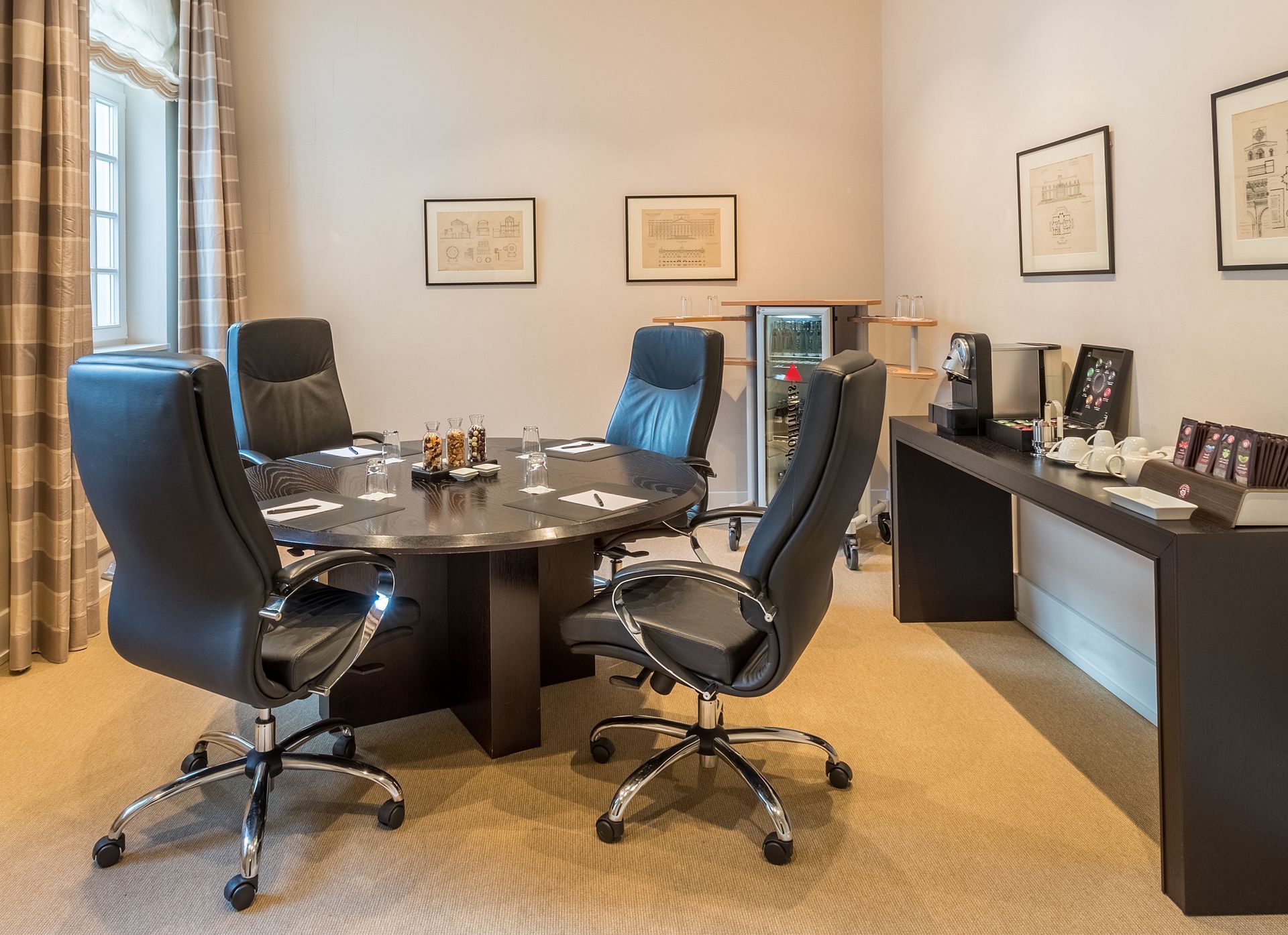 Konferenzraum mit rundem Tisch, schwarzen Ledersesseln und Erfrischungsstation.