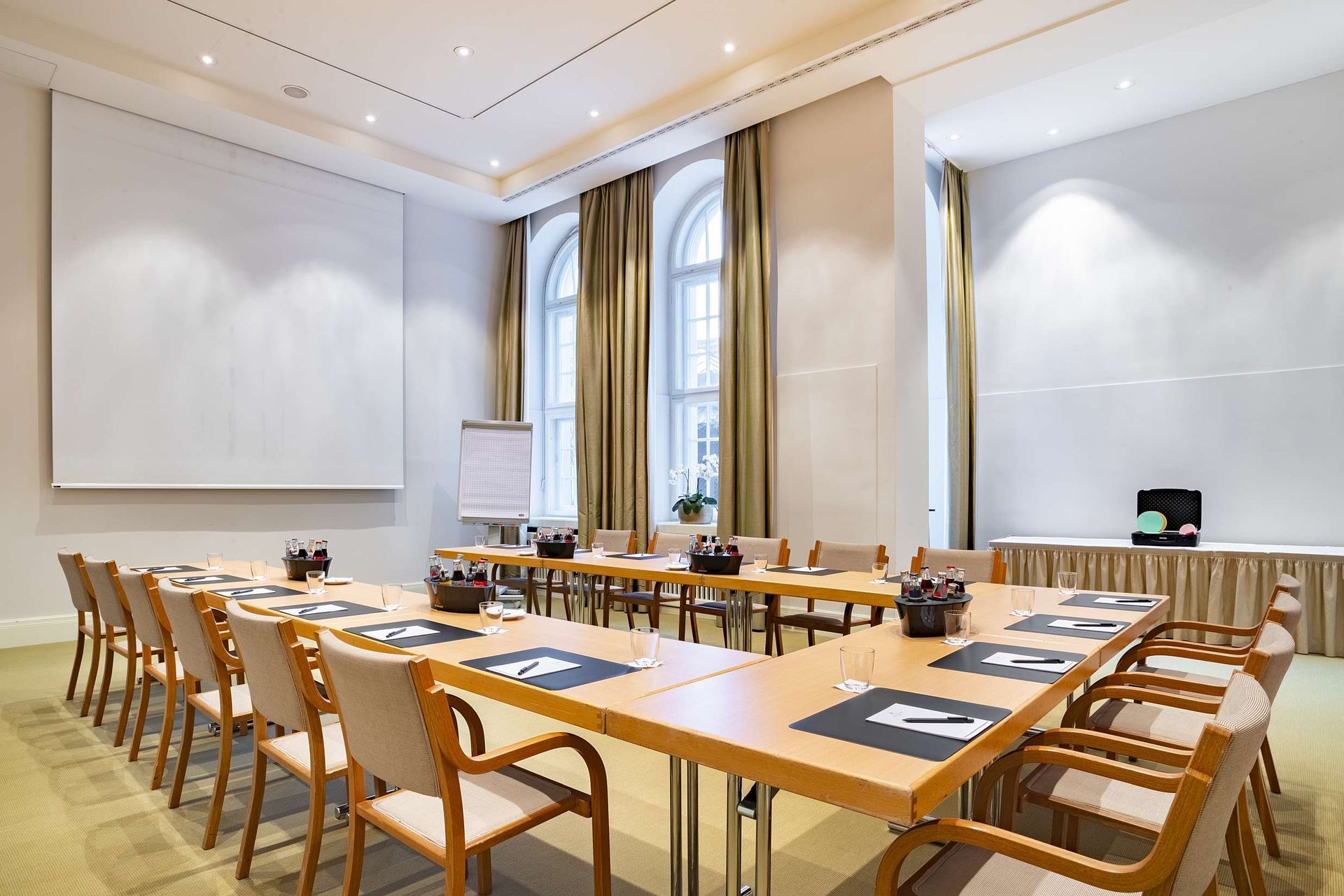 Ein für ein Meeting eingerichteter Konferenzraum mit einem U-förmigen Tisch, Stühlen und großen Fenstern.