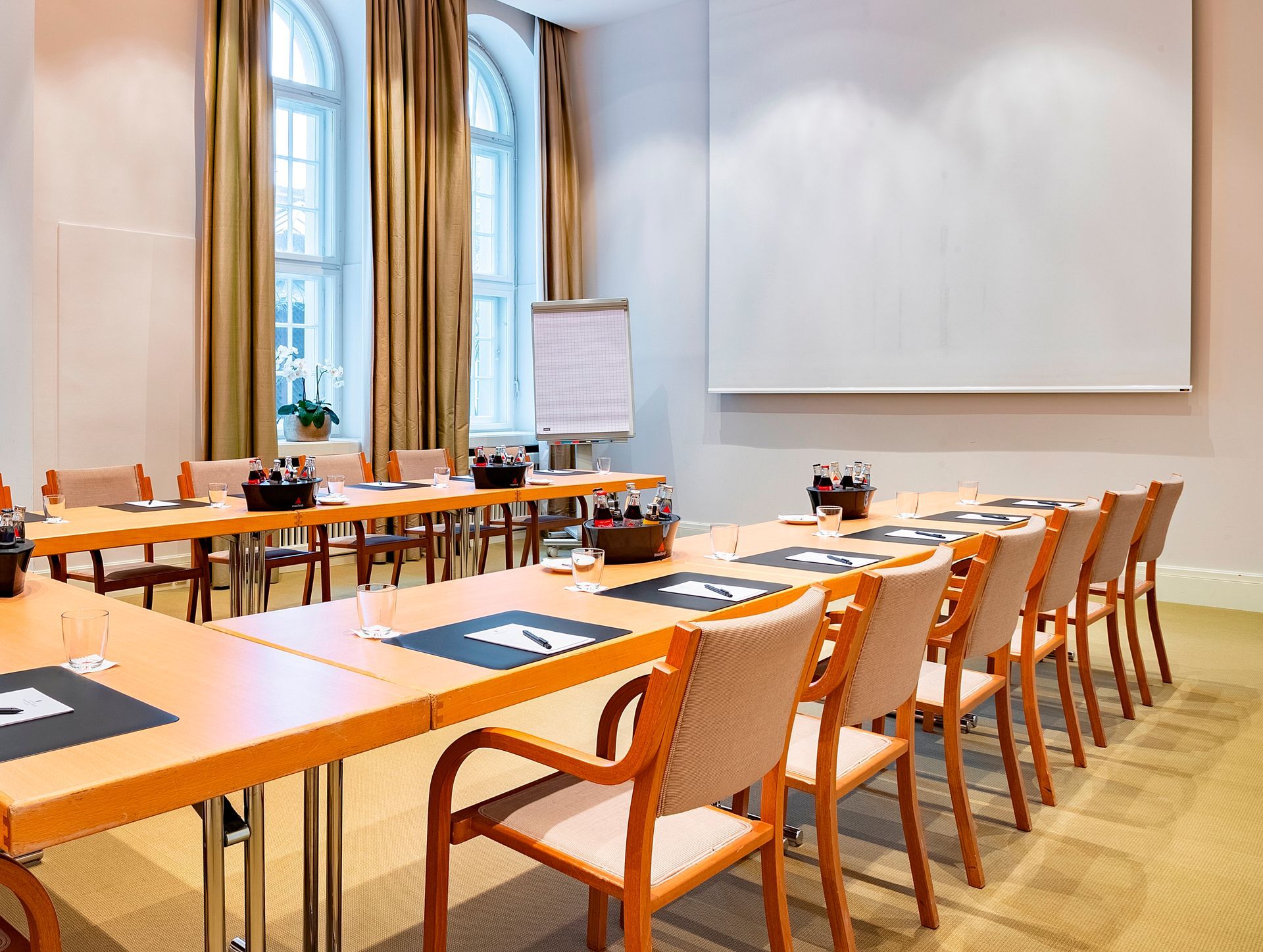 Der Konferenzraum ist mit einem U-förmigen Tisch und Stühlen, einem großen Fenster und einer Whiteboard-Tafel ausgestattet.