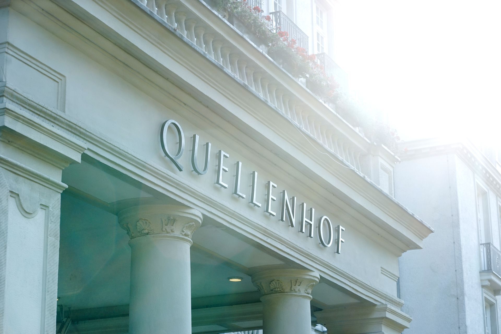 Der Eingang des Hotels Quellenhof in Aachen mit seinen klassischen weißen Säulen und hellem Sonnenlicht darüber.