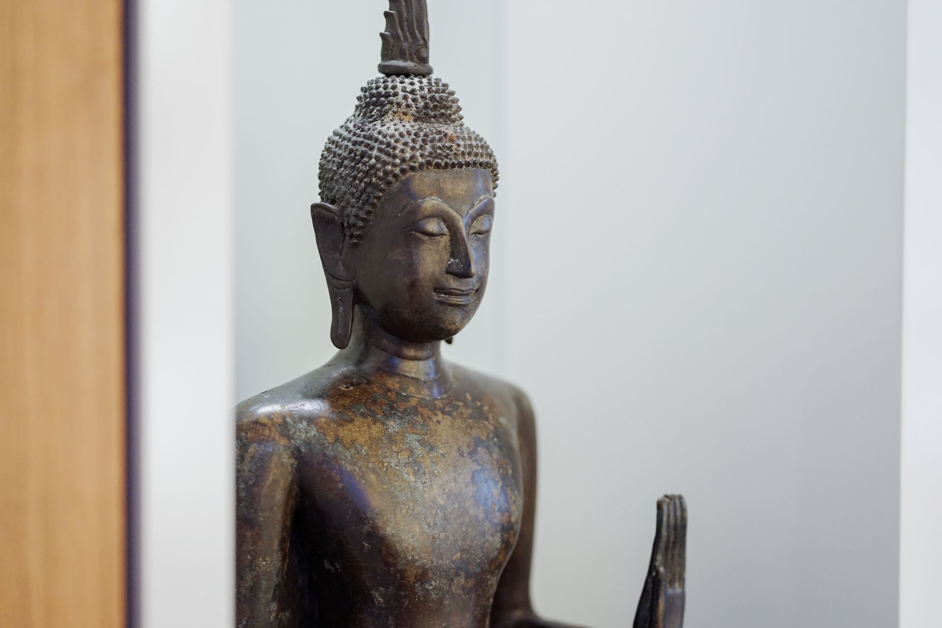 Bronze Buddha statue with closed eyes, outdoors, weathered surface.