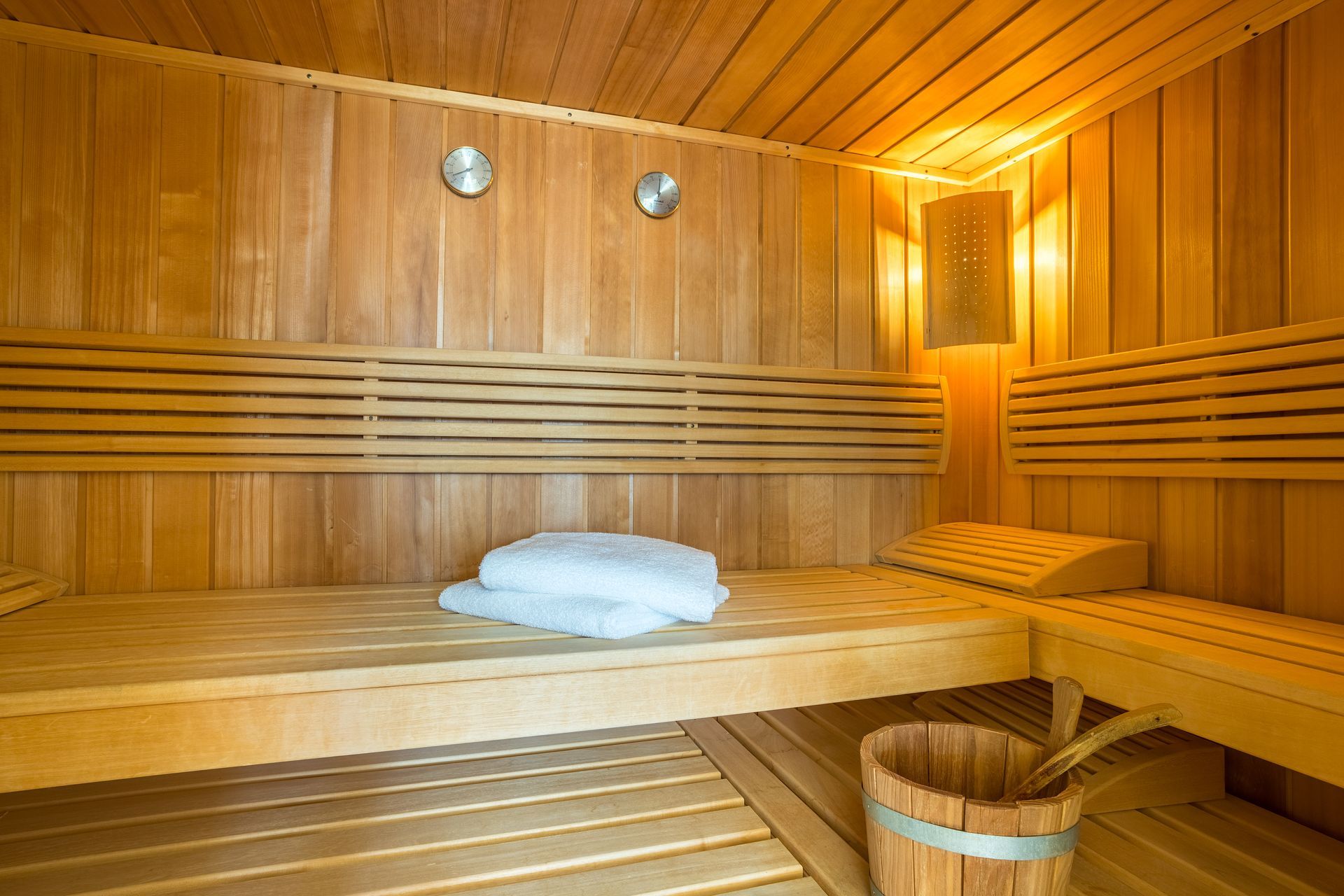 Wooden sauna interior with benches, a bucket, and towels.