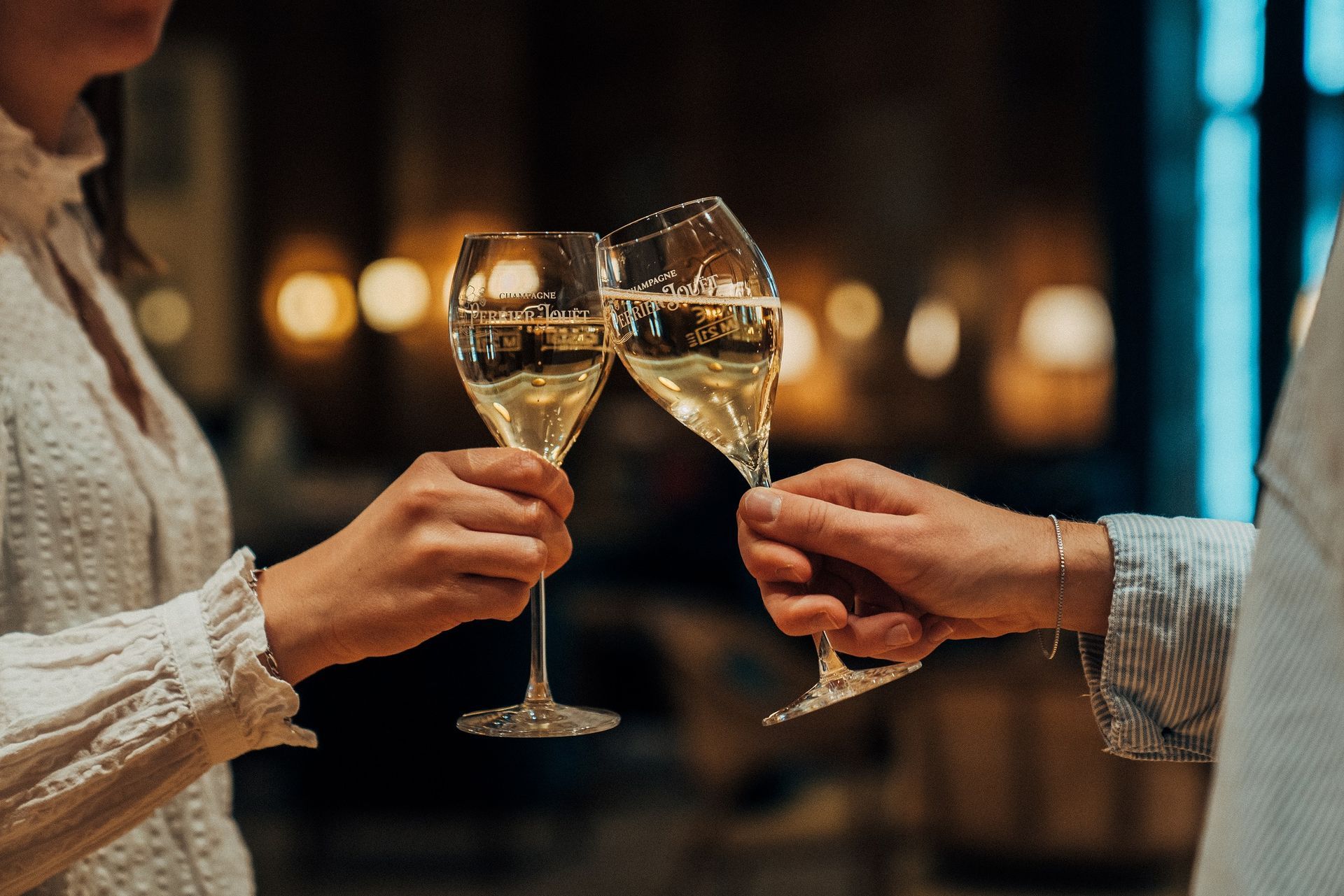 Zwei Personen stoßen mit Champagnergläsern an. Warmes Licht.