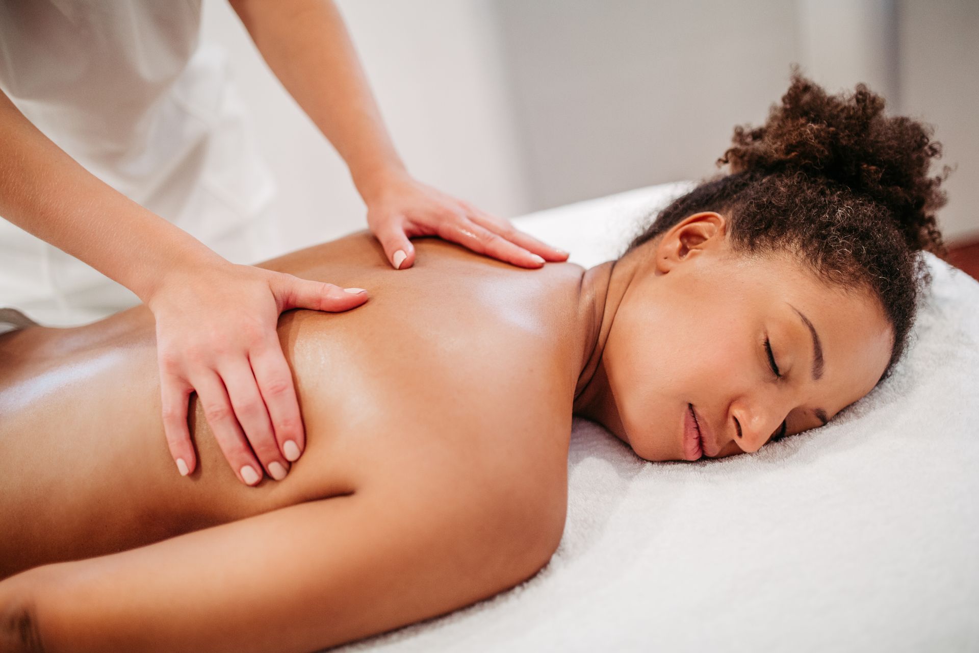 Hände massieren den Rücken einer Person auf einer Massageliege. Die Person liegt mit dem Gesicht nach unten, die Augen geschlossen.