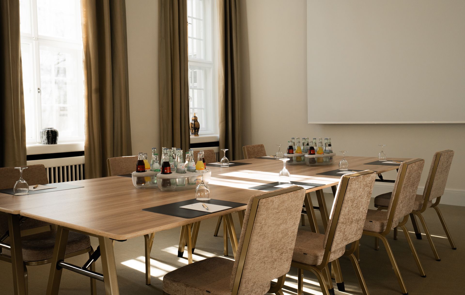 Der Konferenzraum ist mit einem U-förmigen Tisch und Stühlen, einem großen Fenster und einer Whiteboard-Tafel ausgestattet.