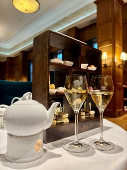 Elegantes Teeservice mit Champagnergläsern und kleinen Snacks auf einer Etagere in einem warm beleuchteten Raum.