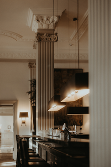 Bar mit hohen Säulen, Hängelampen und Barhockern. Gedämpftes Licht und neutrale Farbtöne.