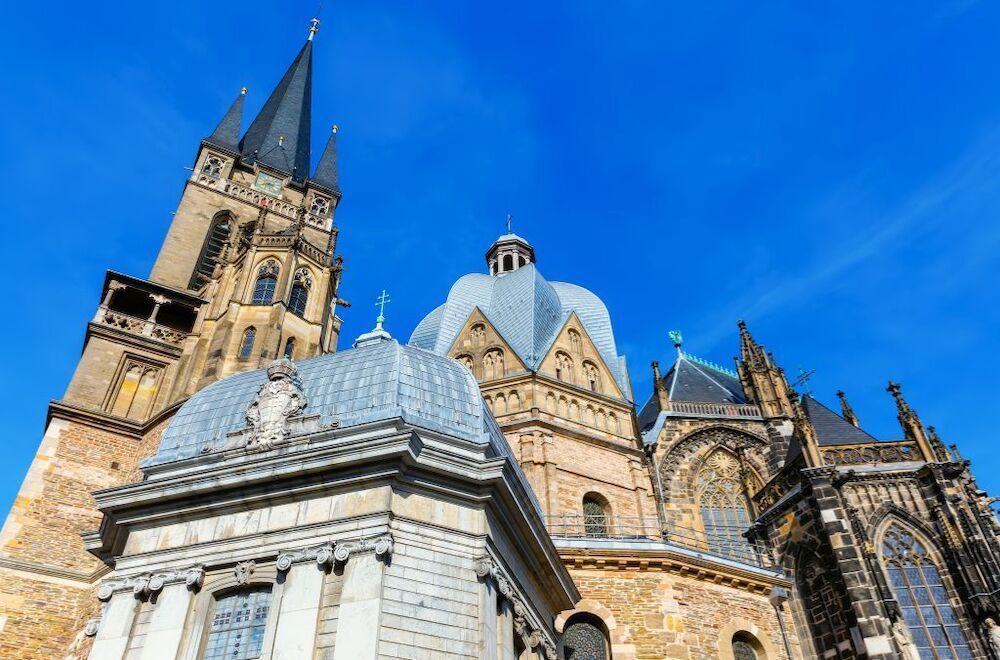 Aachen Cathedral, with its numerous towers and domes, against a bright blue sky.