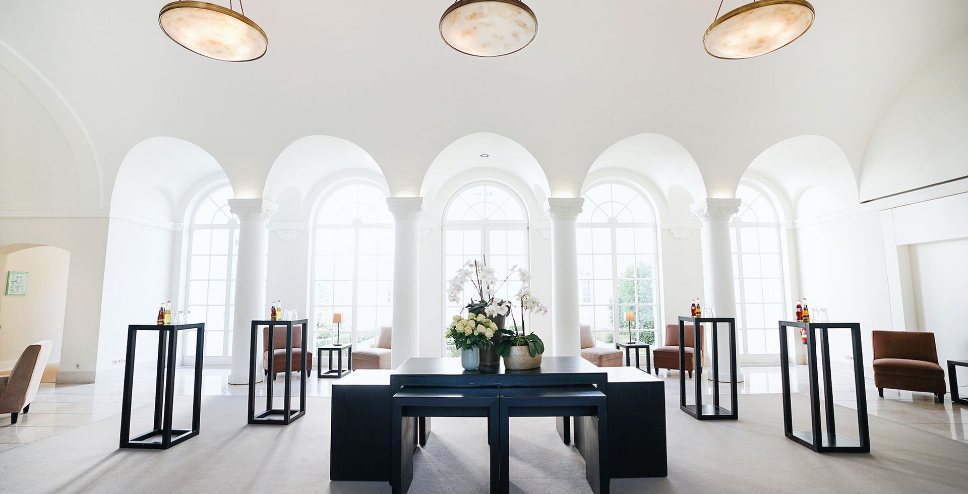 An elegant, white interior with arched windows, tables, and floral arrangements.