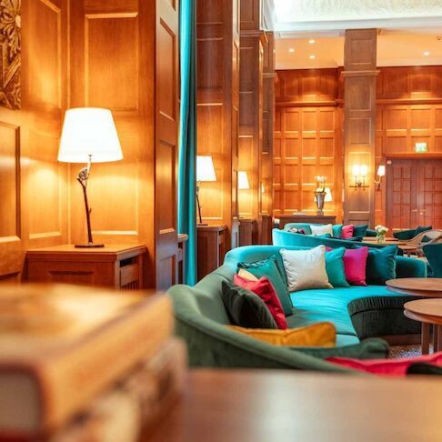 A cozy lounge with a turquoise sofa, wood paneling, lamps, and colorful pillows.