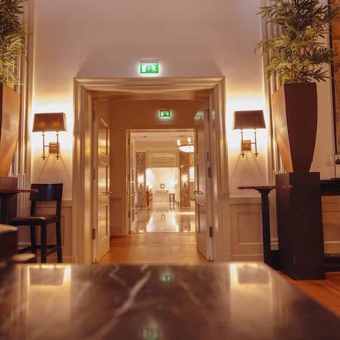 A hotel hallway with an open door, plants, and wall sconces.