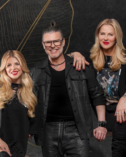 Three smiling people dressed in black are posing in front of a dark, textured background.