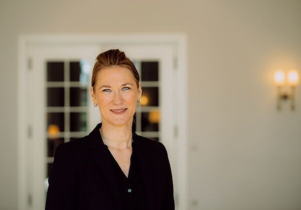 Eine Frau in schwarzem Oberteil lächelt vor einer weißen Tür.