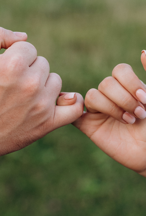 Two hands, with their little fingers intertwined, form a gesture that symbolizes a promise.