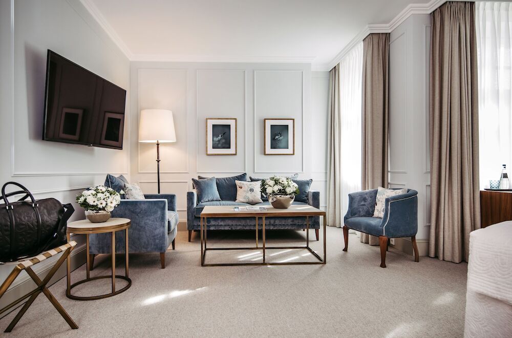 Luxuriöses Wohnzimmer mit blauen Sofas, neutralen Wänden, großen Fenstern und einem an der Wand montierten Fernseher.