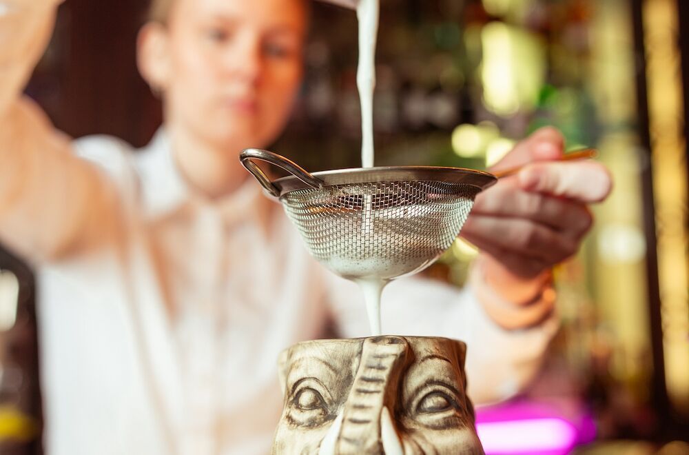 Zwei Personen in weißen Bademänteln halten Champagnergläser verkehrt herum auf einem Bett, Kopf an Kopf.