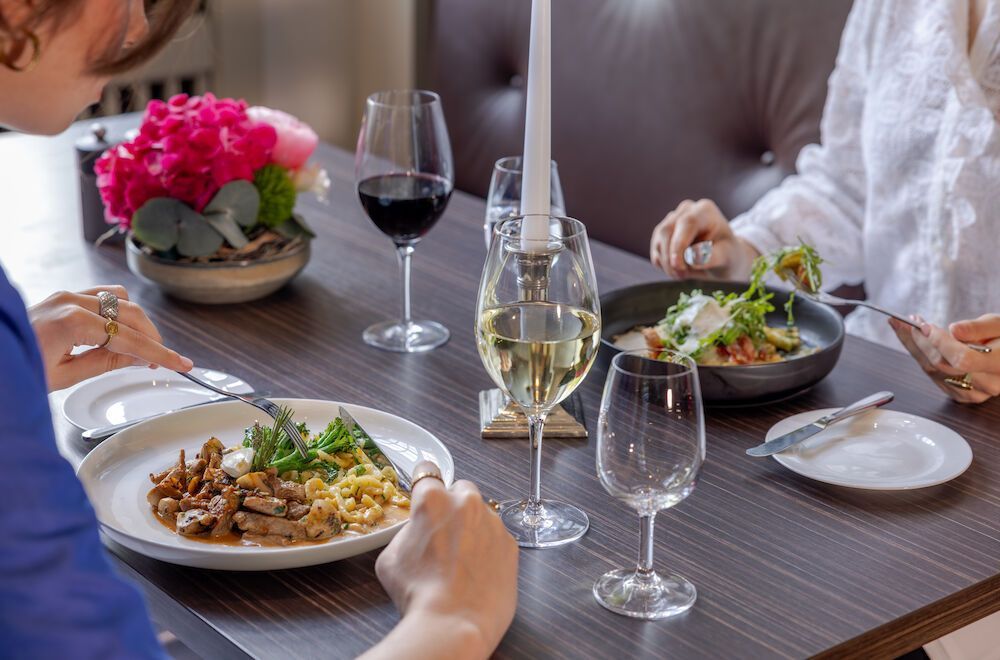 People are dining at a table, enjoying food and wine. An elegant atmosphere, flowers, candlelight.