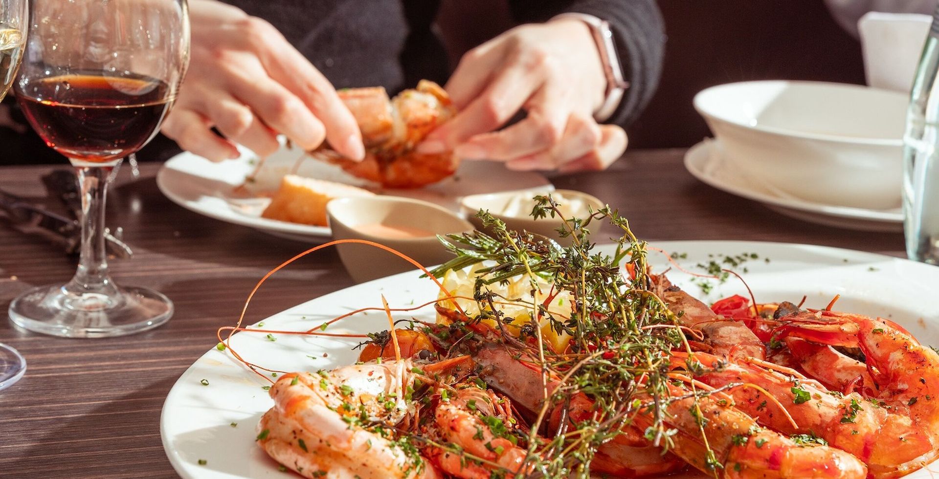 A plate of grilled shrimp and bread; a person reaching for food at a restaurant table.