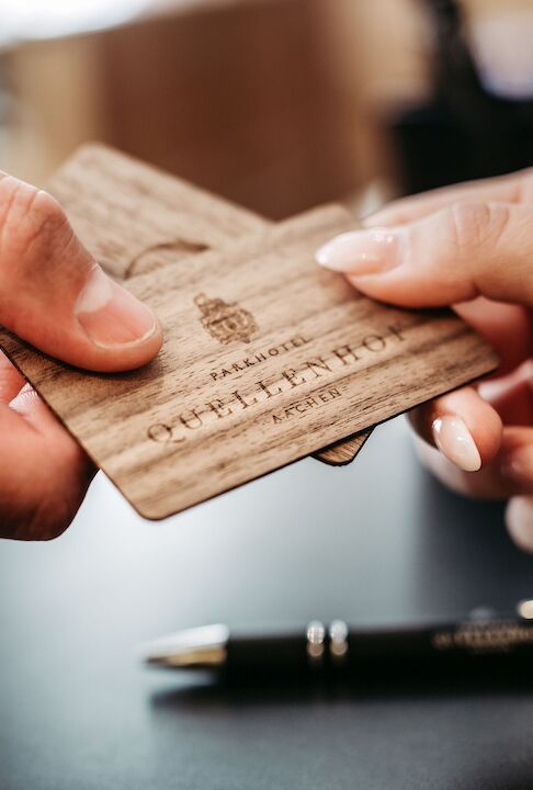 Eine Person übergibt einer anderen hölzerne Hotelzimmerschlüsselkarten. Auf einem Schreibtisch ist ein Stift zu sehen.