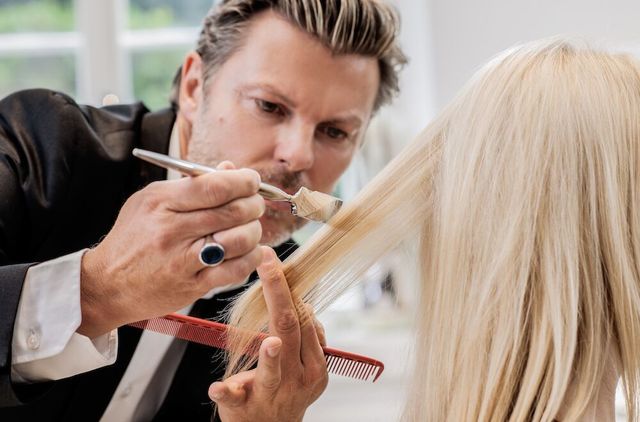 Eine Friseurin schneidet mit Kamm und Schere blonde Haare an einem Übungskopf.
