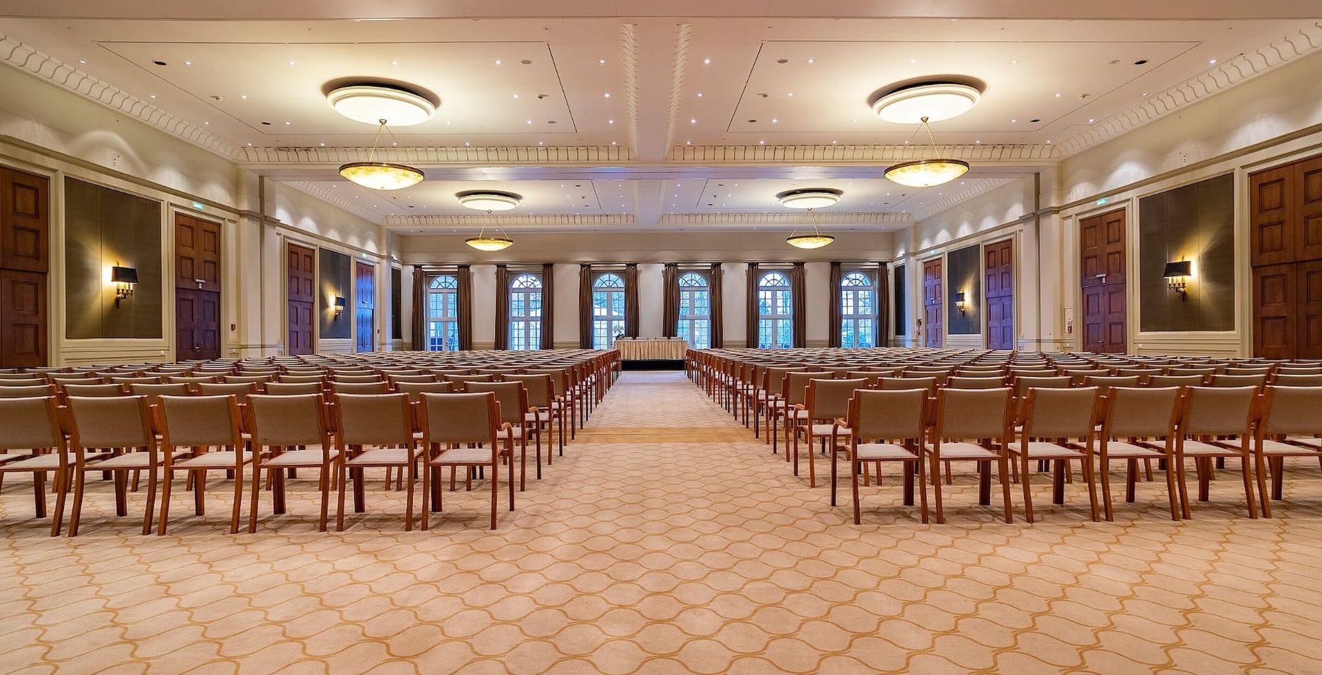 Ein großer, prunkvoller Ballsaal, der für eine Präsentation hergerichtet ist; Stuhlreihen sind auf eine Bühne ausgerichtet; neutrale Farbtöne.