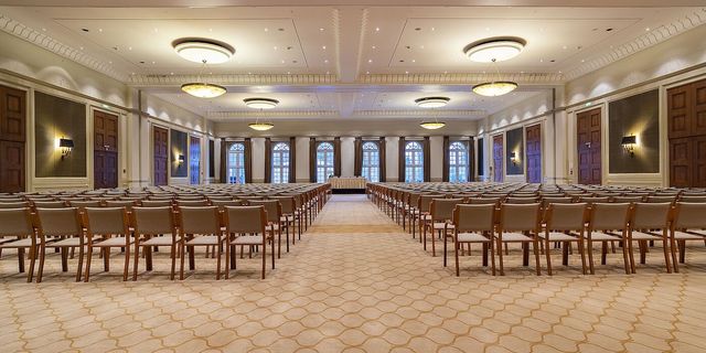 Ein großer, eleganter Ballsaal, der für eine Konferenz oder ein Treffen eingerichtet ist, mit Reihen von Stühlen und Tischen.