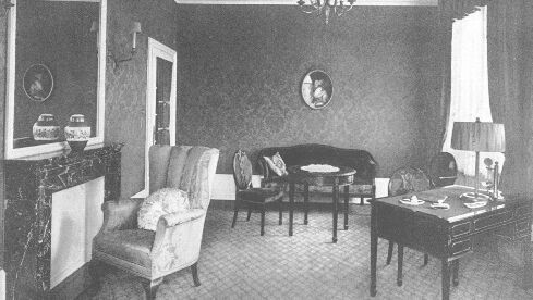 Ein reich verzierter Raum mit Kamin, Sessel, Sofa, Tisch und dunklen Wänden.