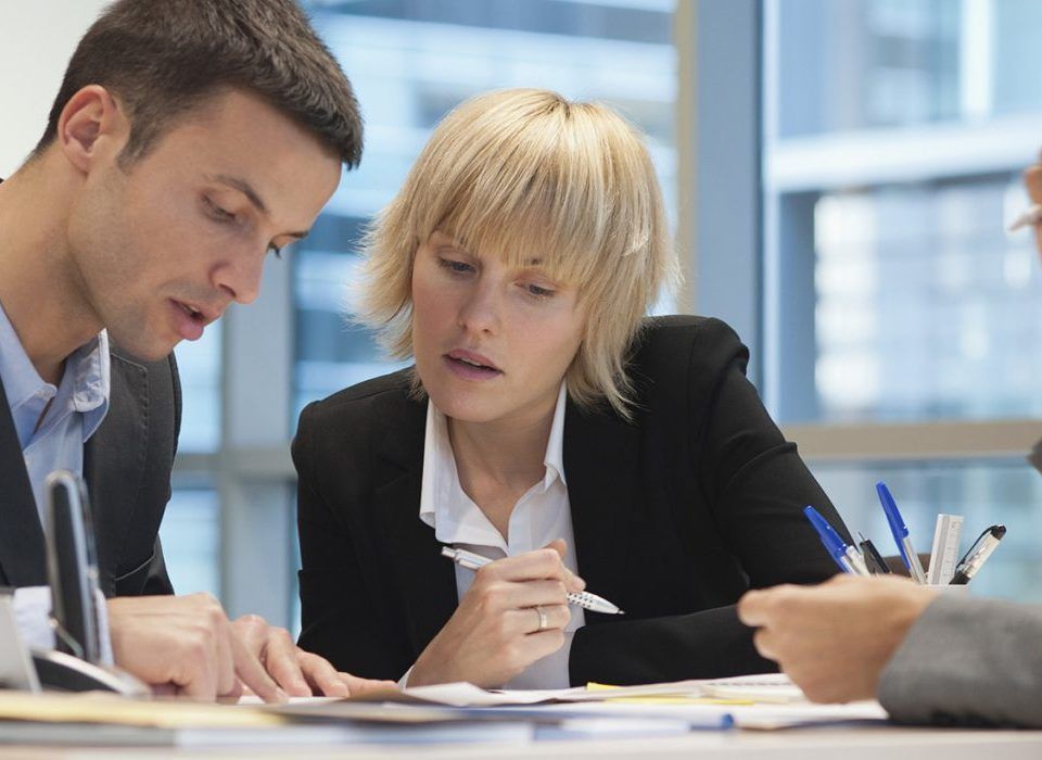Deux personnes en costume examinent des documents dans un bureau et en discutent les détails.