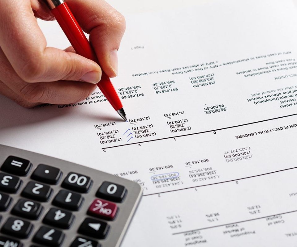 Une main tenant un stylo rouge écrivant sur un rapport financier à côté d'une calculatrice.