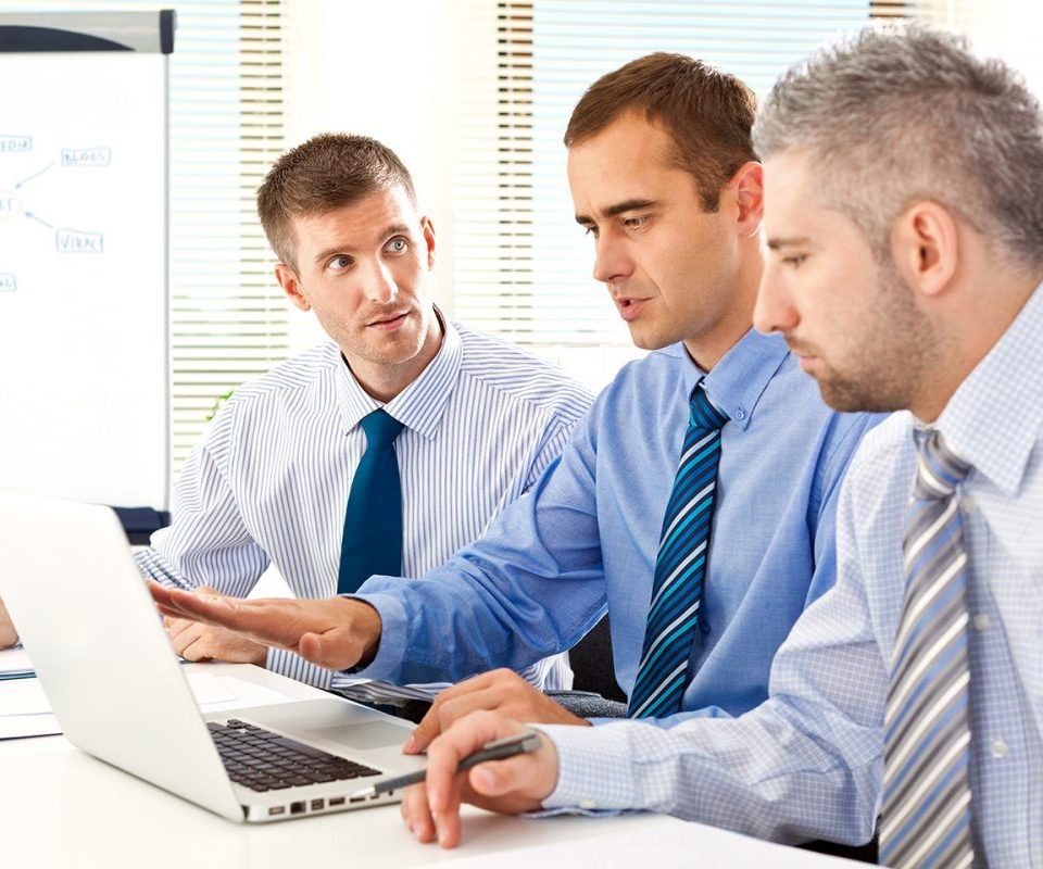 Trois hommes en tenue de ville examinent un écran d'ordinateur portable lors d'une réunion.