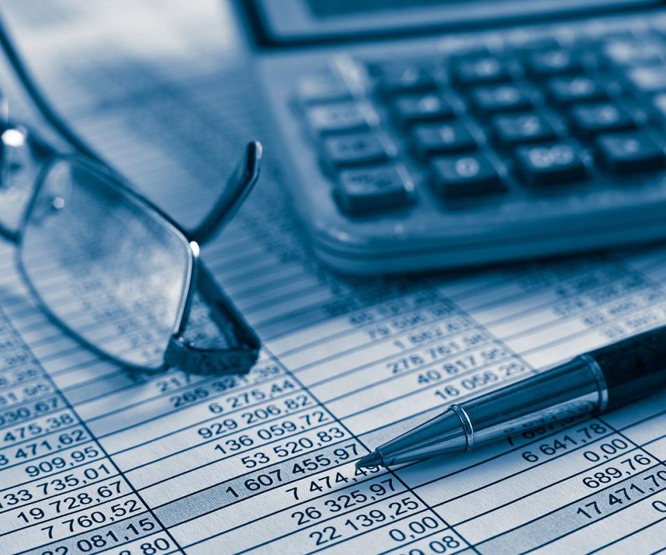 Des documents comptables, une calculatrice, un stylo et des lunettes sur un bureau.