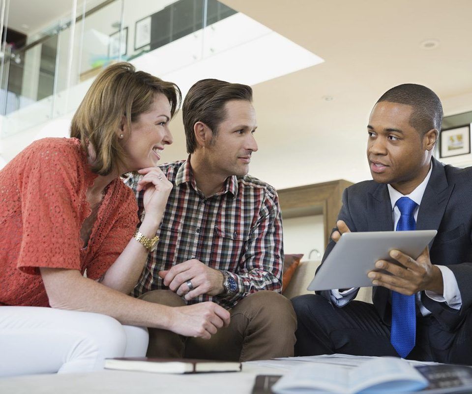 Un couple consulte un conseiller financier, les yeux rivés sur une tablette, à l'intérieur.