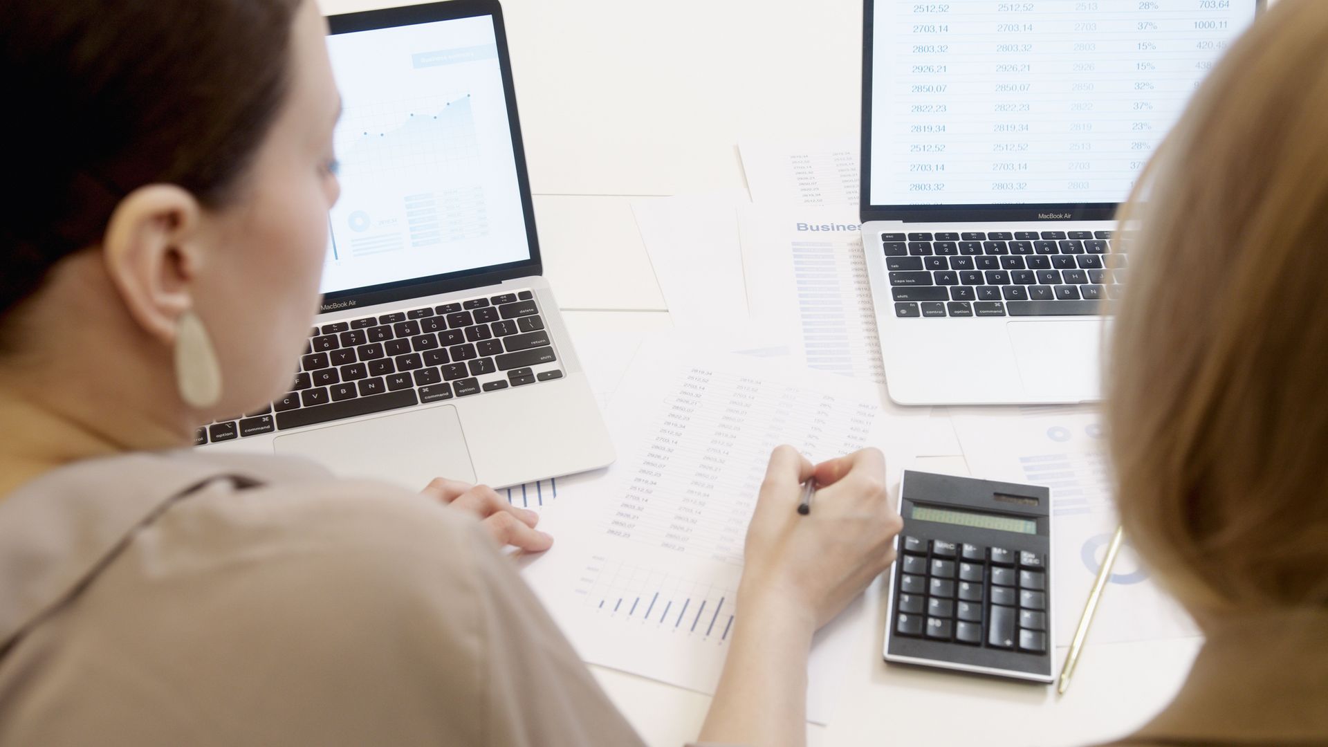 Deux personnes consultent des tableurs sur des ordinateurs portables avec une calculatrice sur un bureau blanc